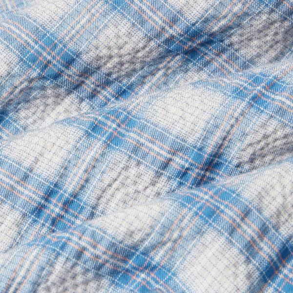 A close-up of a plaid fabric with a white base, blue stripes, and thin orange and gray lines forming a checkered pattern.