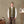 Load image into Gallery viewer, A man stands in a studio wearing an olive green zip-front vest over a white long-sleeve shirt, brown trousers, and black shoes. The background features a warm beige wall, a wooden desk with art supplies, and an easel with a painting.
