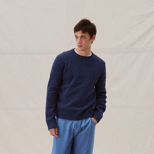 man looking to the left wearing wide jeans and dark blue jumper on beige background