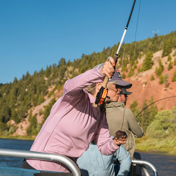 woman fly fishing from boat wearing pink jumper