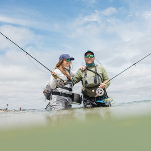 Two people fishing in a body of water with a clear sky above.