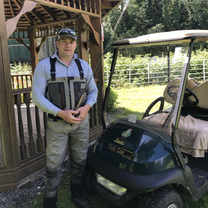 man stading next to buggy wearing waders and holding fly rod