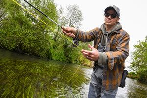 Man fly fishing by a river with trees in the background