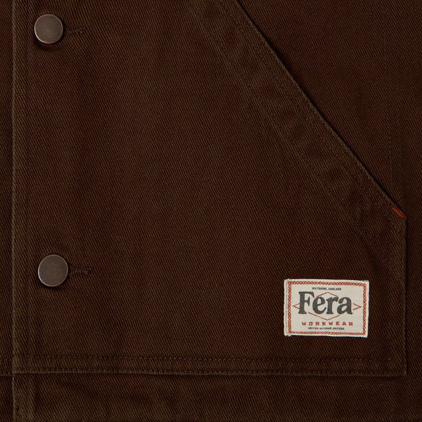 Close-up of a dark brown canvas jacket featuring a diagonal flap pocket with metal snap buttons and a small Fera Norway label.