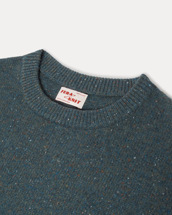 Close-up of a ribbed crewneck sweater in a heathered blue-gray color with subtle multicolor flecks, featuring a visible 'FRA-KNIT' neck label.