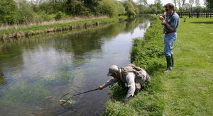 Man on the River Test bank, catching a fish with a net, whilst another man watches