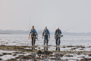 three men walking through water wearing fly fishing clothing
