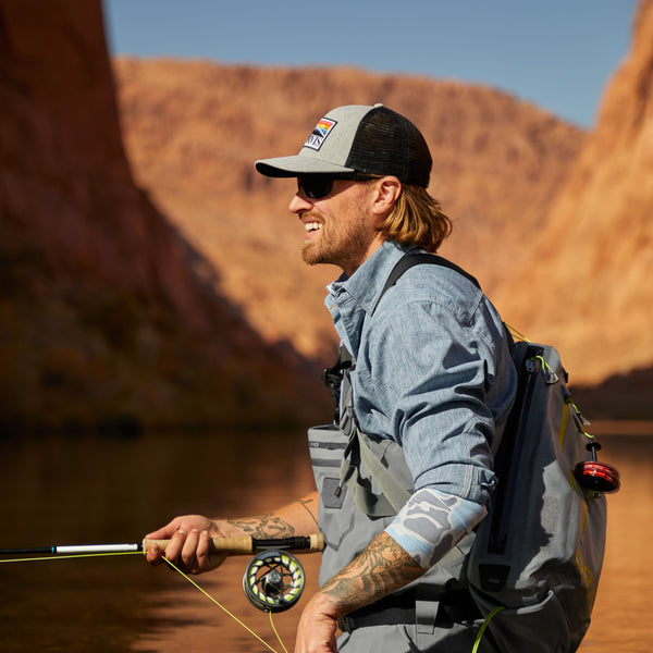 Side view of a man wearing fishing gear in the mountains, in the sunshine, smiling